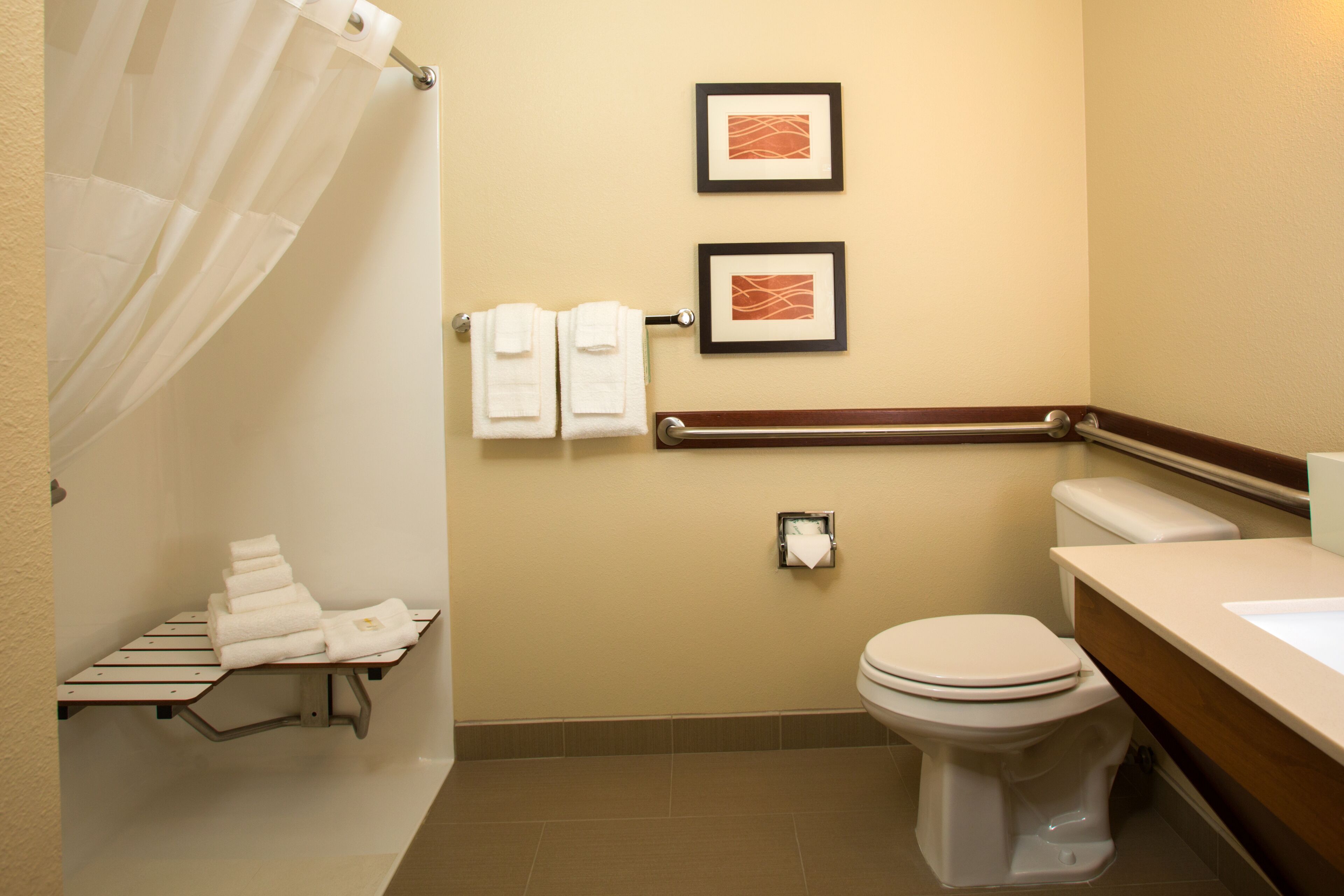 Une salle de bain équipée de toilettes, d’un lavabo, d’un porte-serviettes et de tableaux encadrés accrochés au mur.