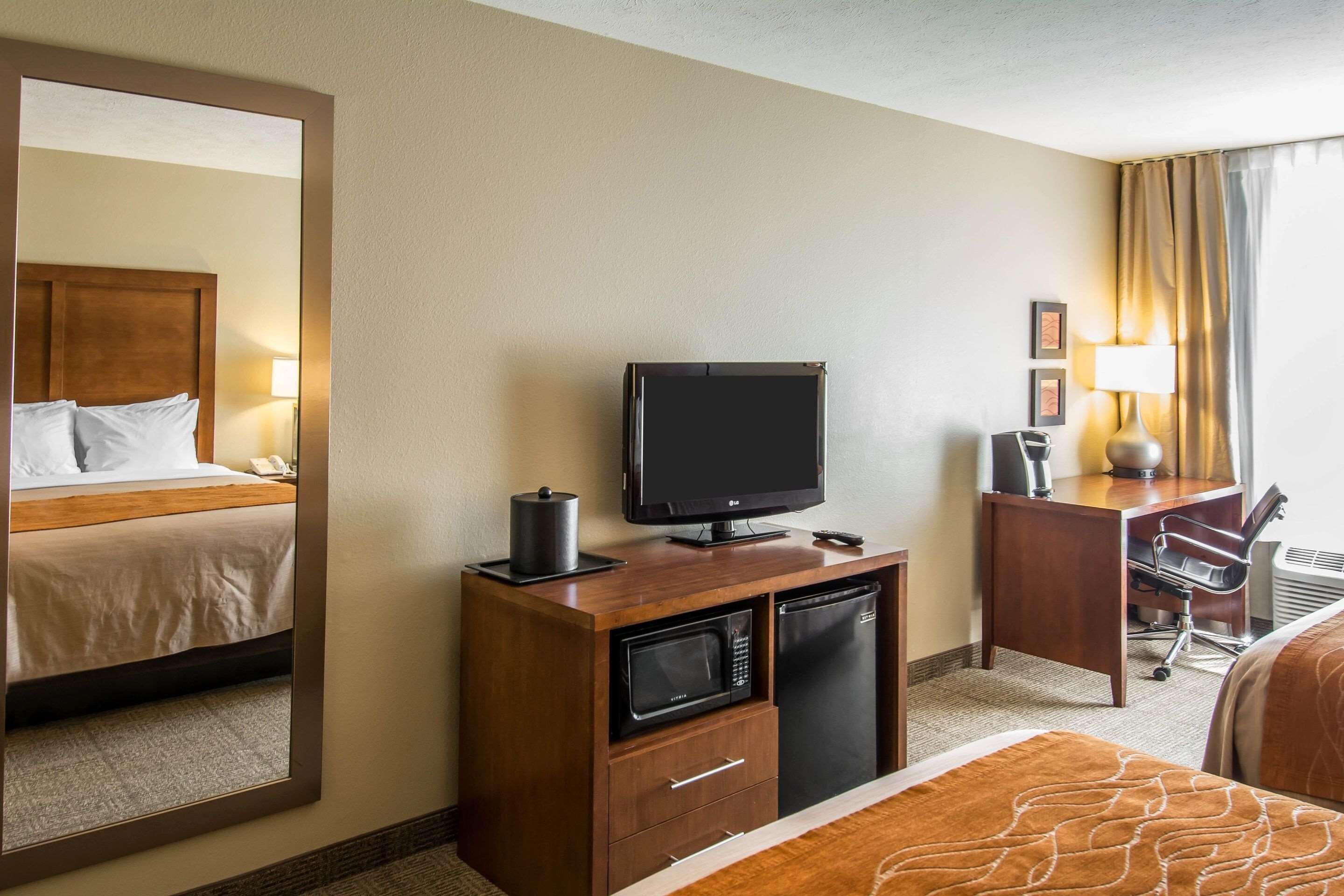 A hotel room with a bed, a desk with a computer, a television, a microwave, and a refrigerator.