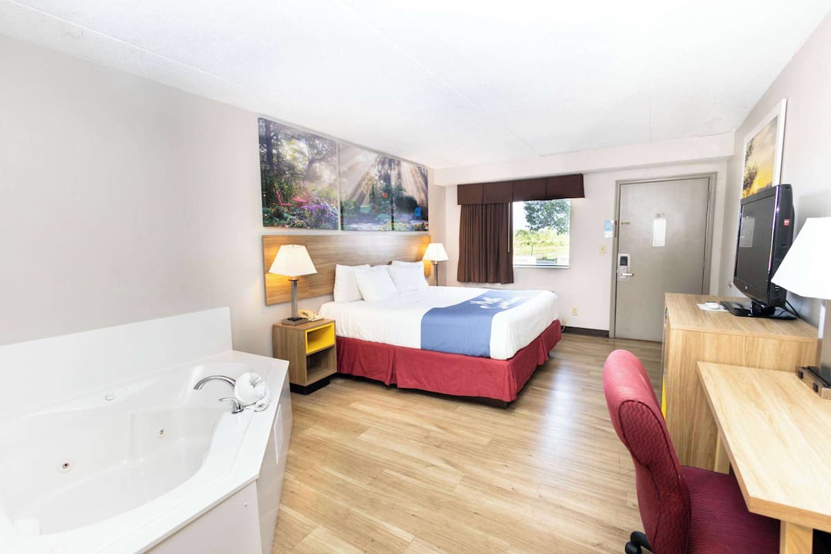 Habitación de hotel con una cama grande, un escritorio, un televisor, un baño con bañera y un cuadro en la pared.