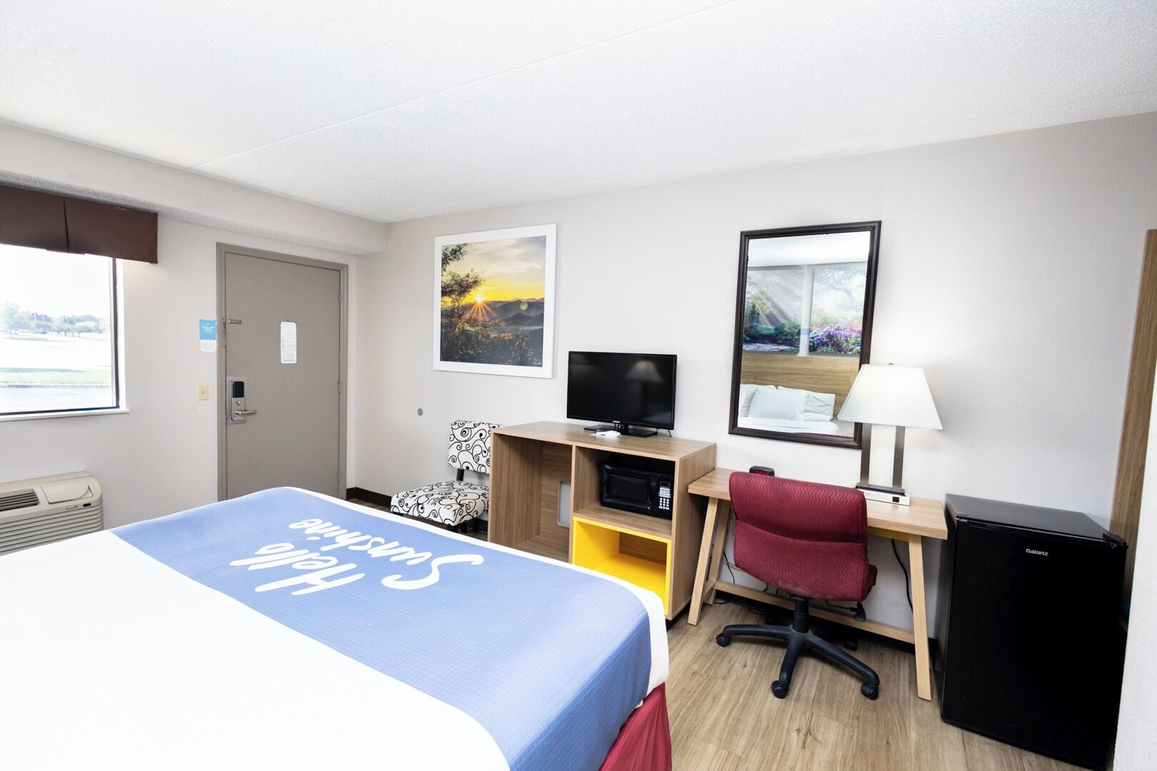 Une chambre d’hôtel équipée d’un lit, d’un bureau, d’une chaise, d’une télévision, d’une lampe et d’un petit réfrigérateur.