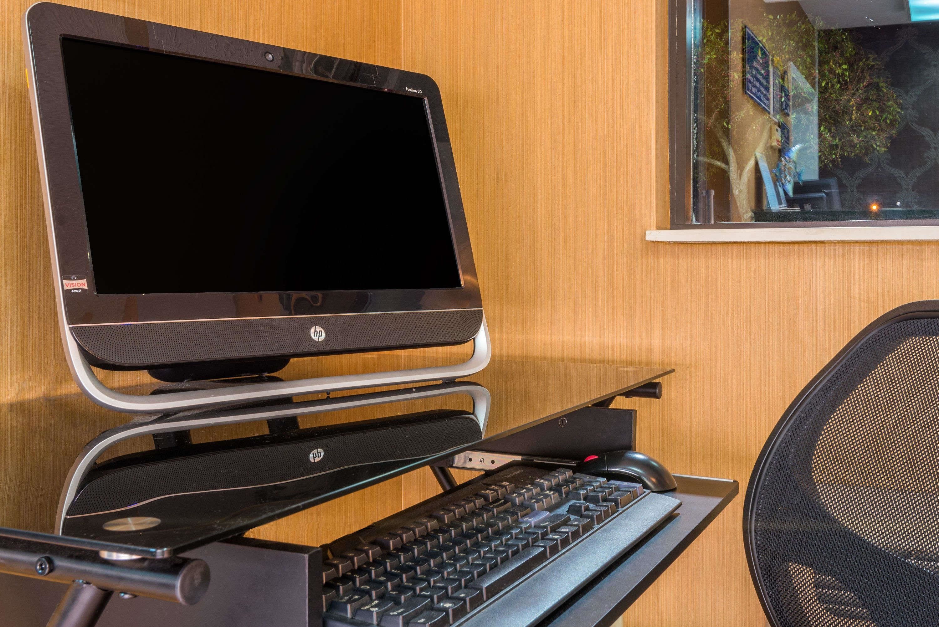 A laptop on a stand with a keyboard, a chair, and a window with a view of trees and a building.