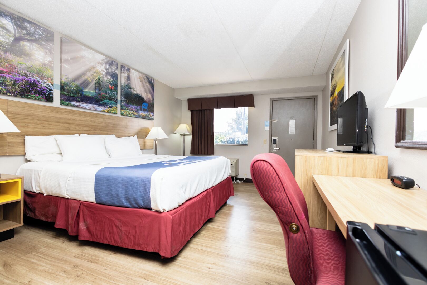 Una habitación de hotel con cama, escritorio, silla, televisor y obras de arte en las paredes.