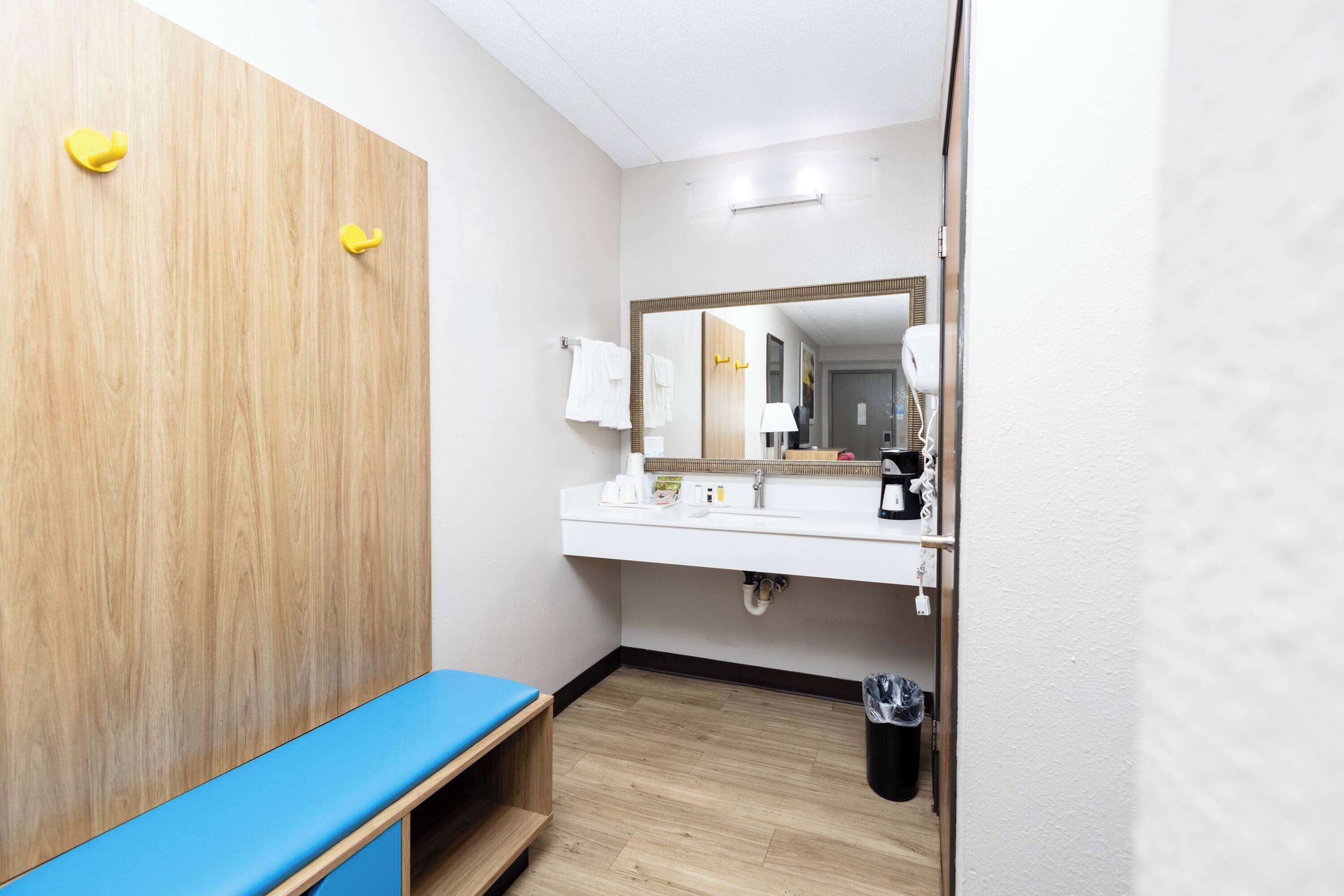 A hotel bathroom with a wooden vanity, a sink with a mirror, and a trash bin.