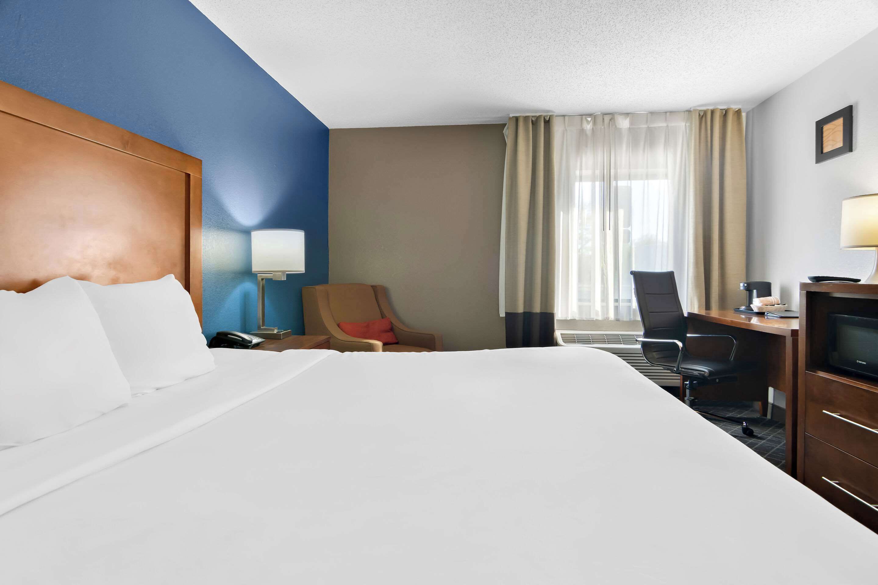 Habitación de hotel con una cama grande, un escritorio con silla, televisor y ventana con cortinas.