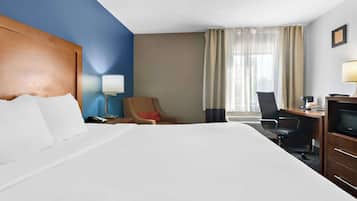 Habitación de hotel con una cama grande, un escritorio con silla, televisor y ventana con cortinas.