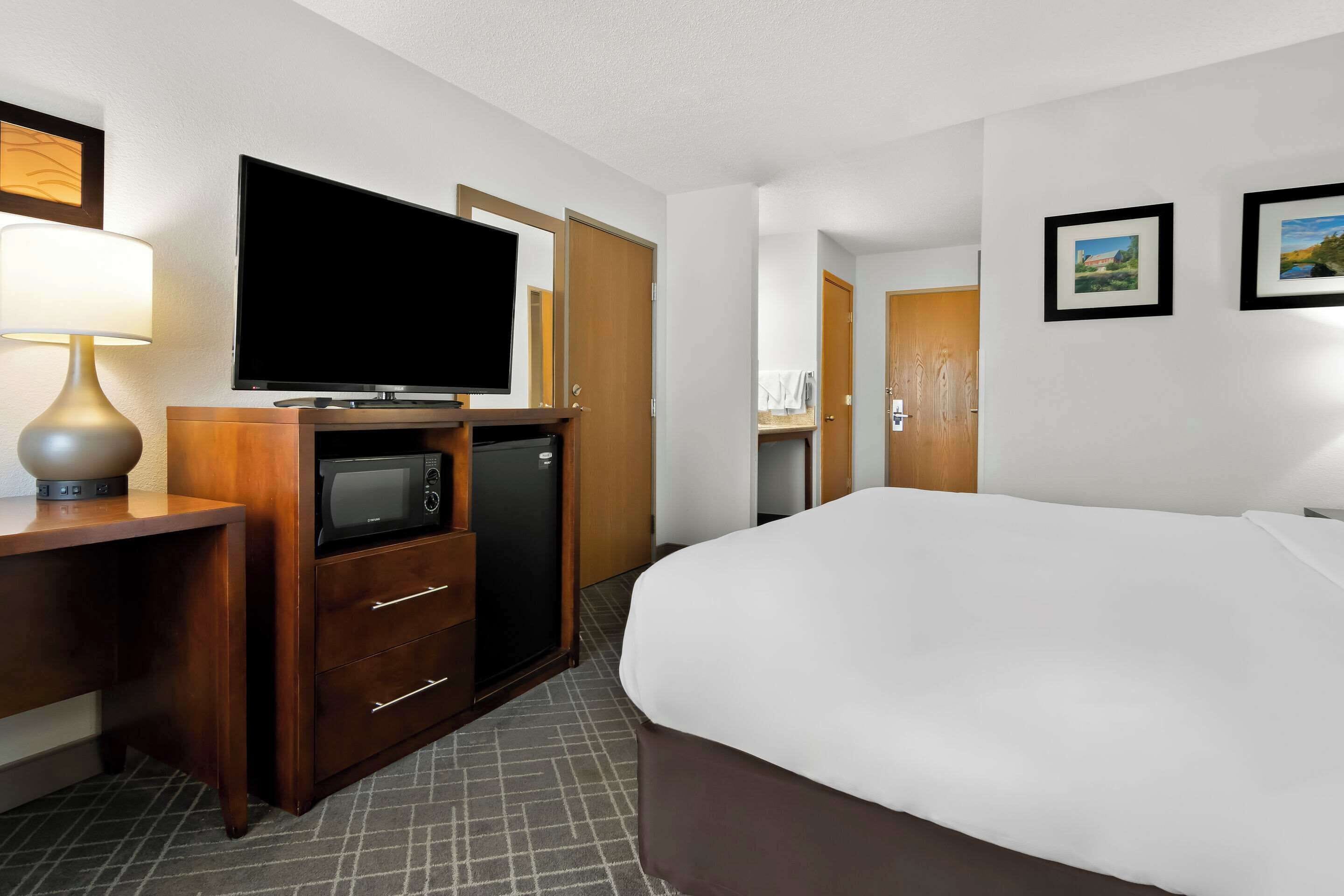A hotel room with a bed, a TV, a microwave, a mini fridge, a desk, and a lamp.