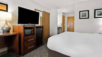 A hotel room with a bed, a TV, a microwave, a mini fridge, a desk, and a lamp.