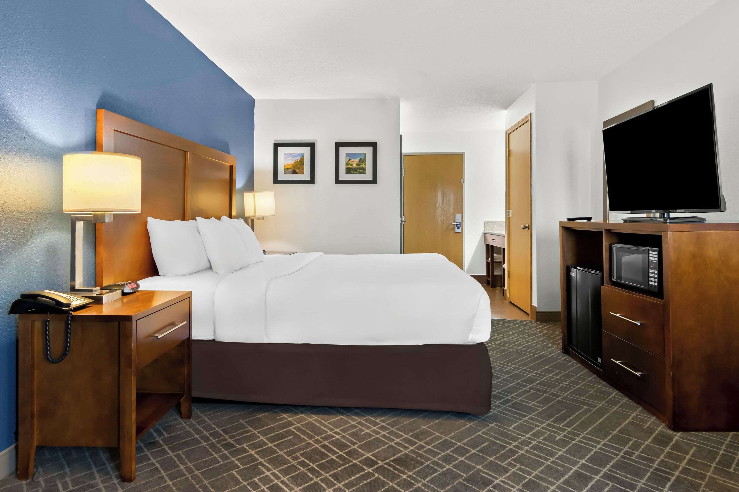 A hotel room with a bed, bedside tables, a TV, a microwave, and a door leading to the bathroom.