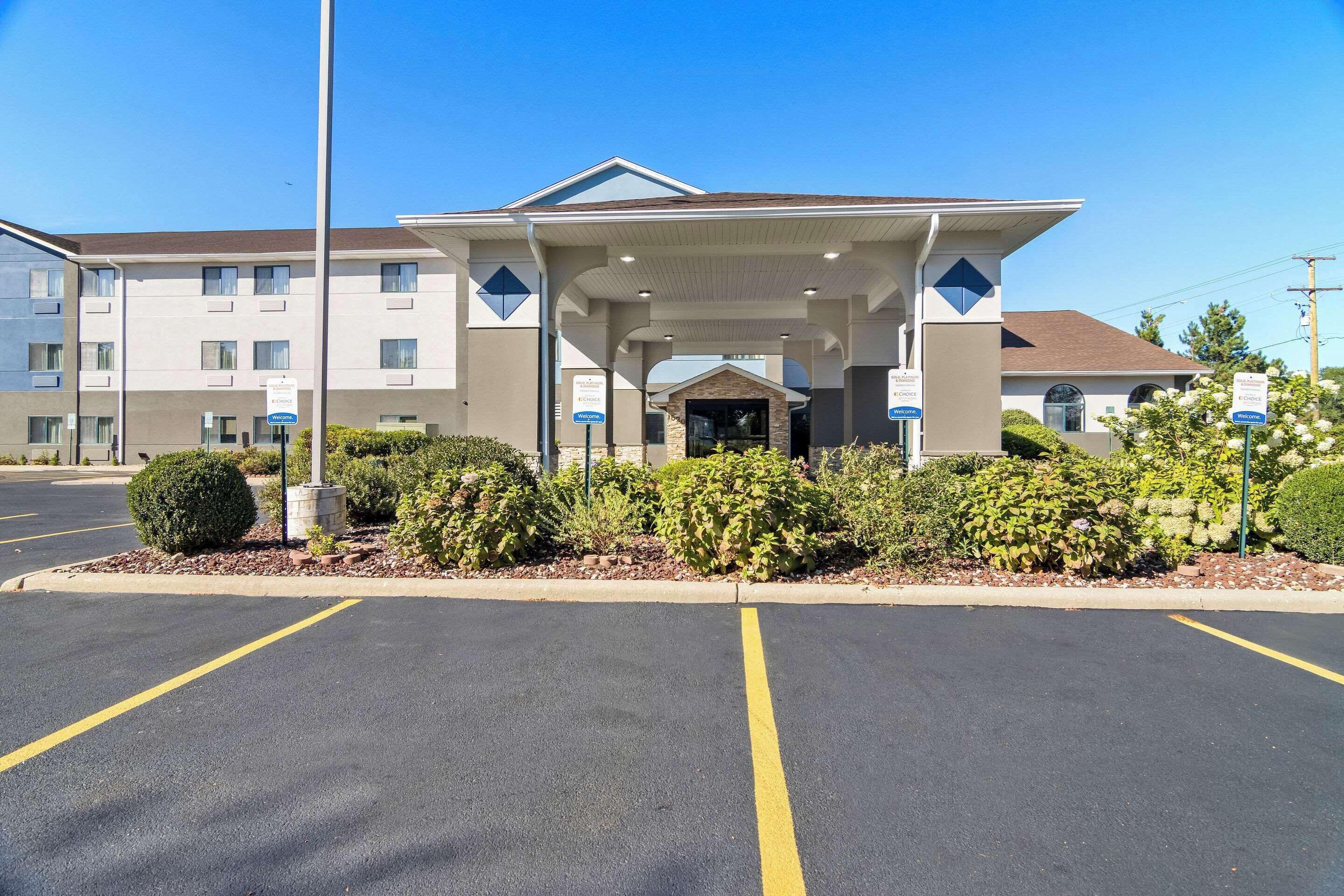 L’entrée d’un hôtel avec un espace de stationnement couvert, un bâtiment doté de nombreuses fenêtres et une signalétique indiquant les équipements disponibles.