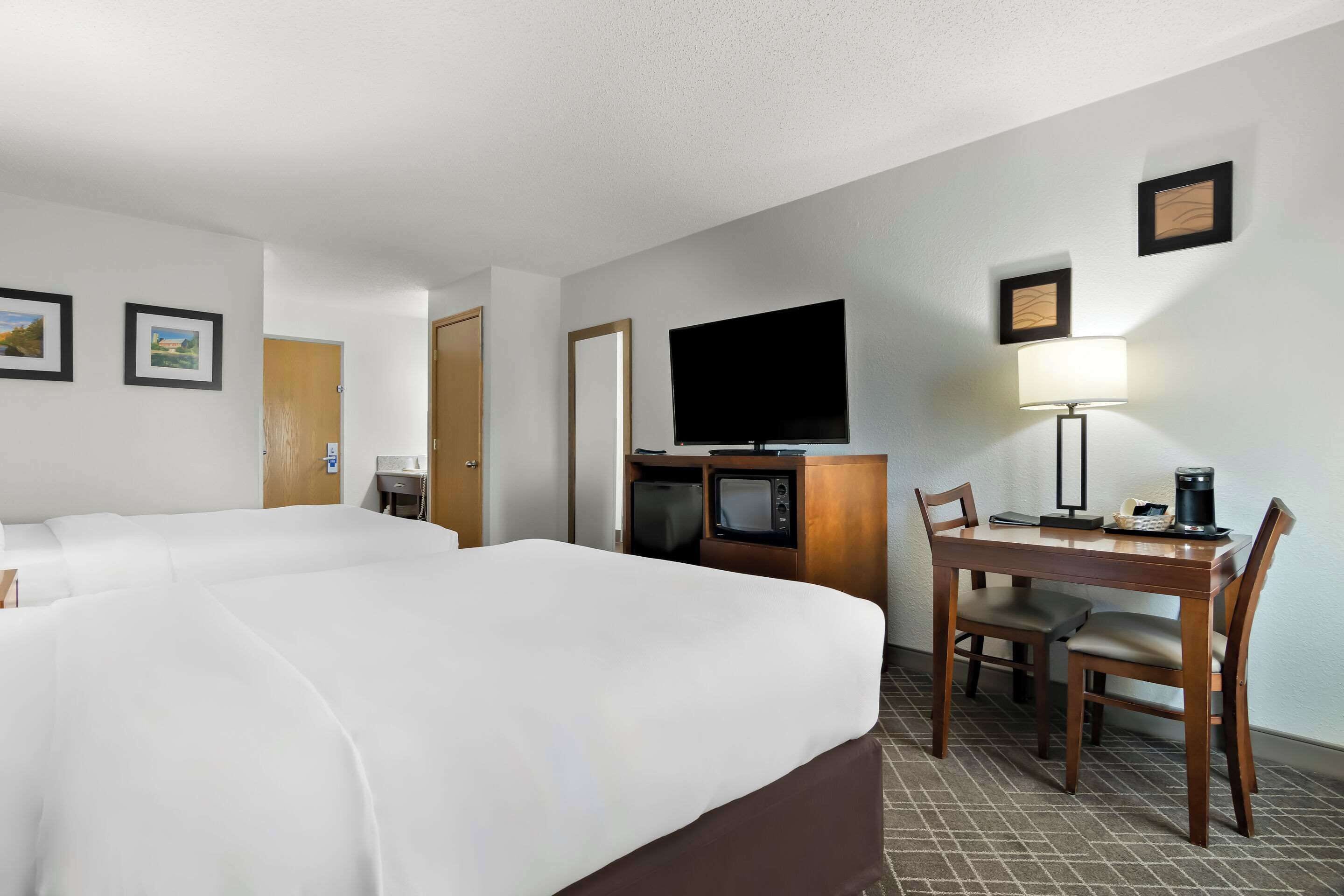 Habitación de hotel con dos camas, televisión, escritorio con lámpara y cafetera.