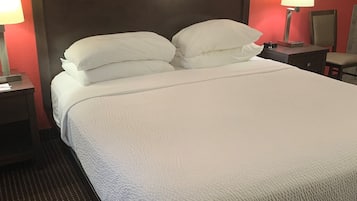 Un letto ben rifatto con lenzuola e cuscini bianchi, una testiera scura e due abat-jour.