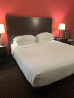 Una cama bien hecha con sábanas y almohadas blancas, un cabecero oscuro y dos lámparas de noche.