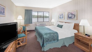 Una habitación de hotel con cama, televisión, escritorio con silla y ventana con vista al agua.