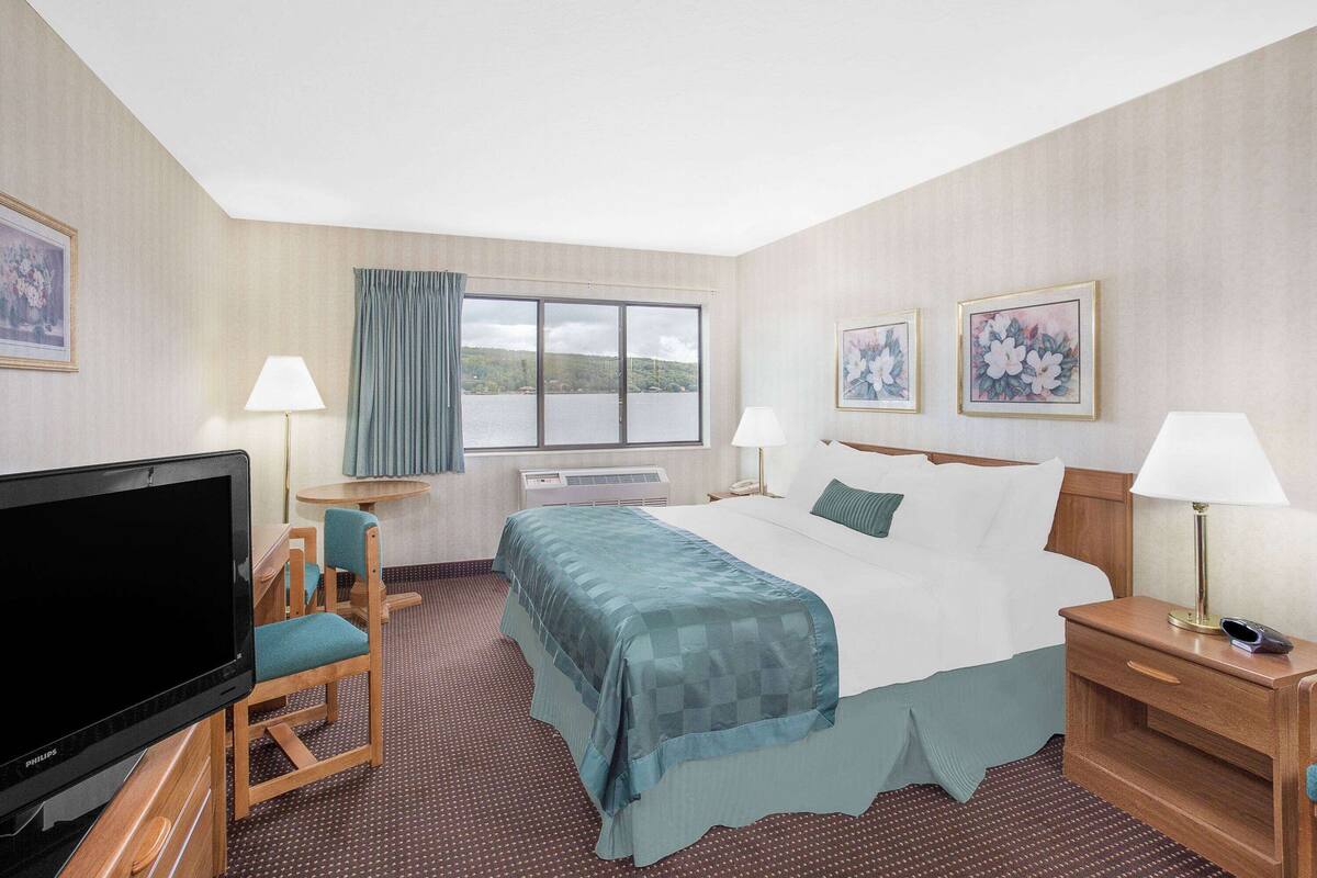 A hotel room with a bed, a television, a desk with a chair, and a window with a view of a body of water.