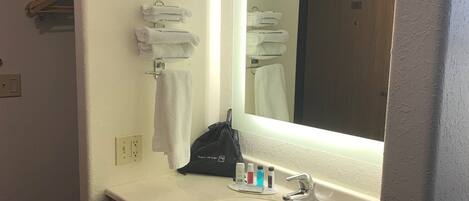 Un baño de hotel con lavamanos, espejo y toallero.