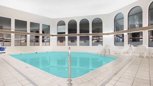 Una piscina interior con agua cristalina, rodeada de suelo de baldosas blancas y sillones de relax blancos.