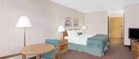A hotel room with a bed, two bedside tables with lamps, a small round table, a chair, and a television.