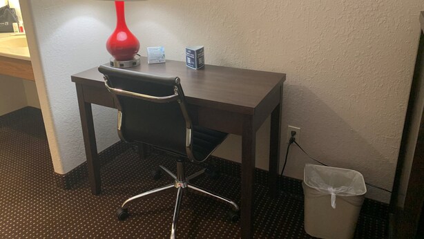 A hotel room with a desk, a chair, a red lamp, a trash bin, and a sign on the wall. - Ramada by Wyndham Hancock Waterfront (Hancock)