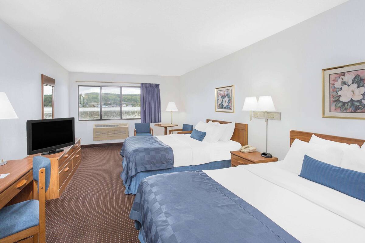 A hotel room with two beds, a desk, a television, and a window with a view of a body of water.
