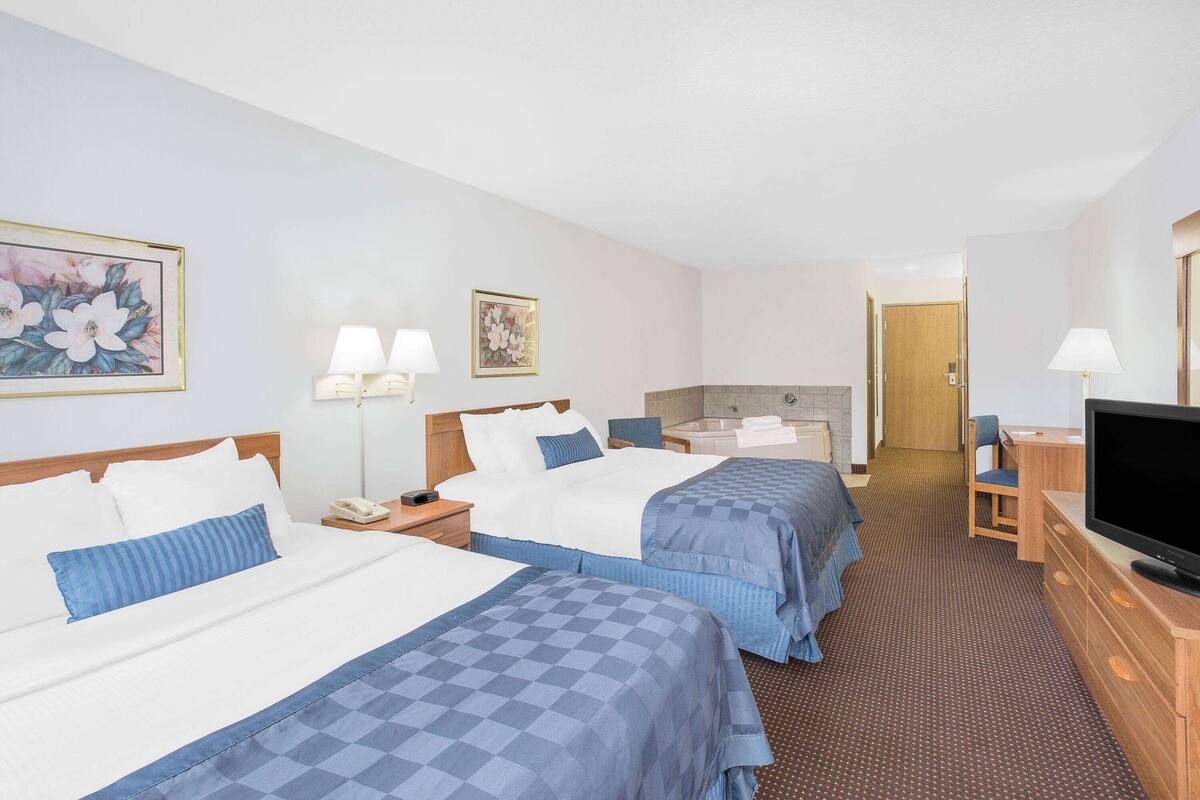 A hotel room with two beds, a television, a desk, and a bathroom.