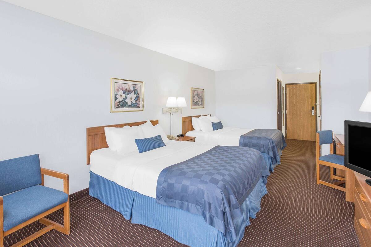 A hotel room with two beds, a TV, a desk, and a chair.