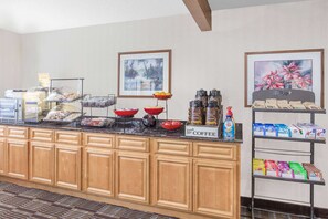 A breakfast bar with various food items and beverages, wooden cabinets, and framed artwork on the walls. - Ramada by Wyndham Hancock Waterfront (Hancock)