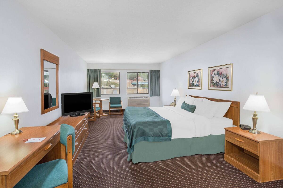 A hotel room with a bed, desk, chair, TV, and two lamps.