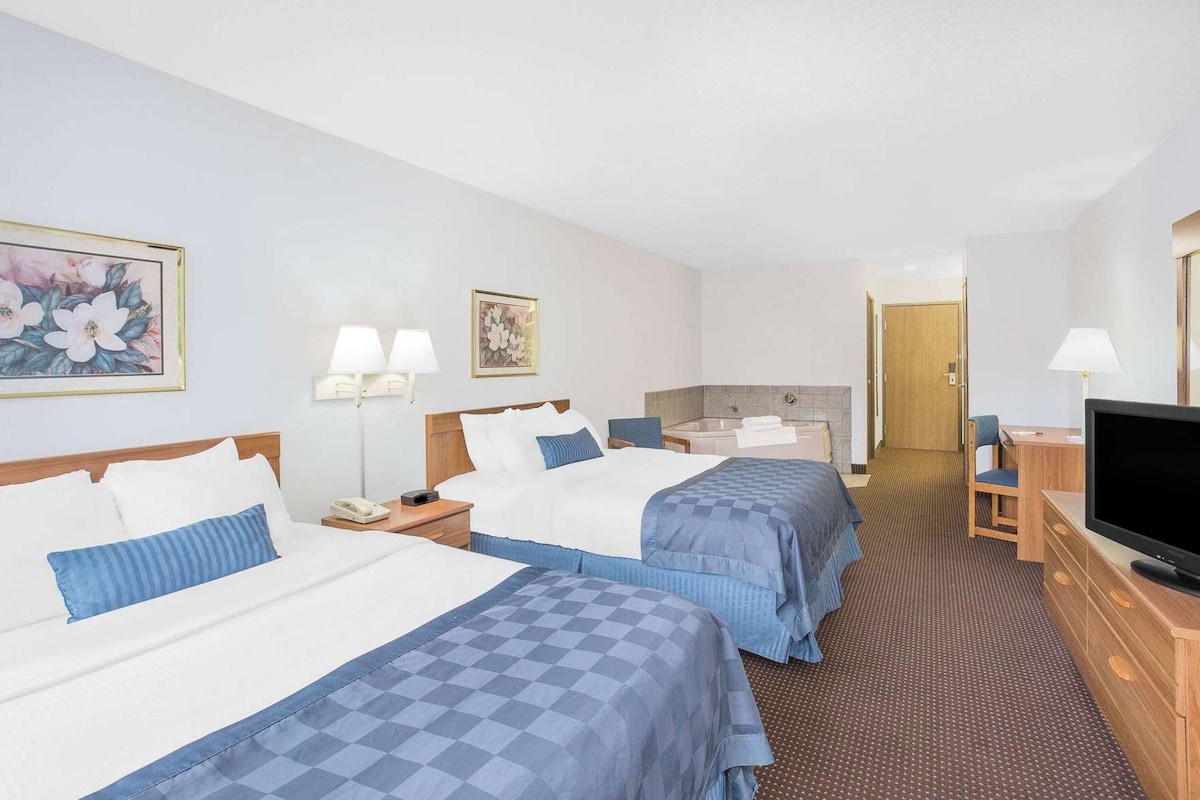 A hotel room with two beds, a desk, a TV, a bathroom, and a painting on the wall.