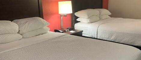 A hotel room with two beds, a nightstand with a lamp, and a red accent wall.