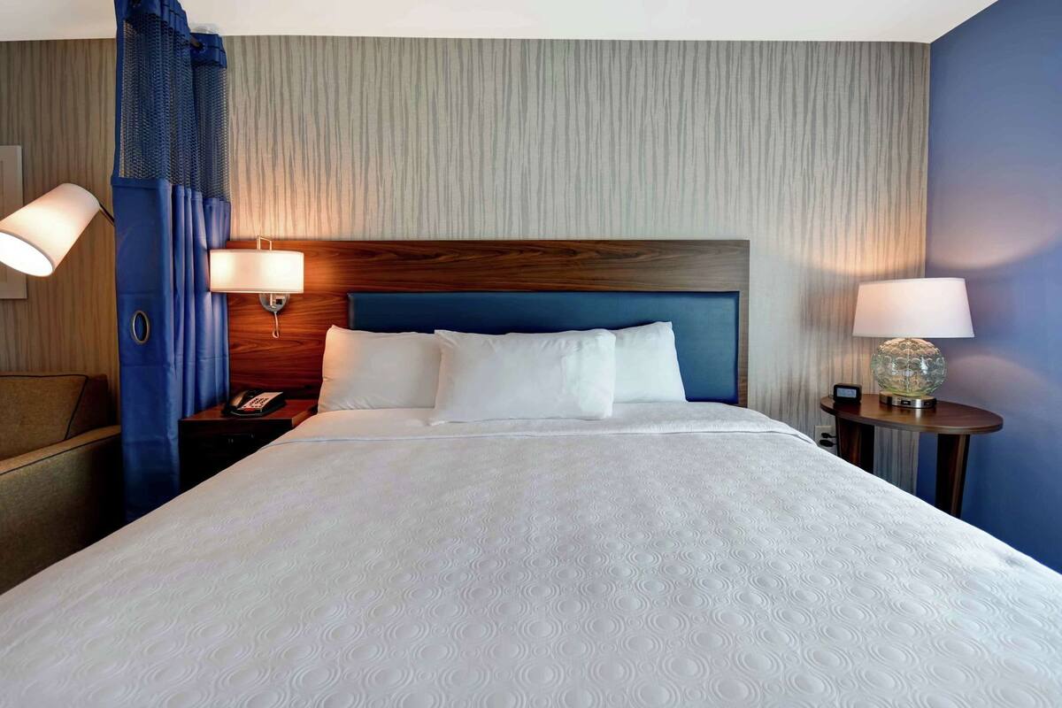 A hotel room with a large bed, two bedside tables, a nightstand, and a wall-mounted lamp.