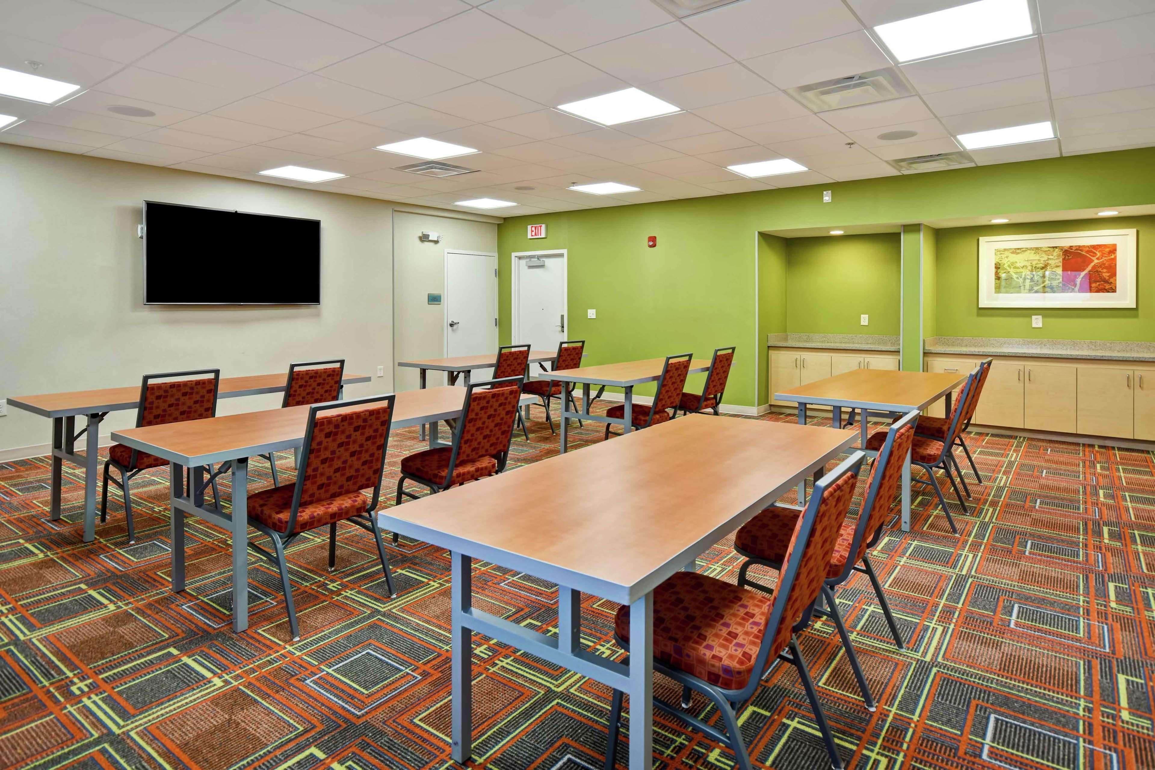 Une salle de conférence dotée de plusieurs tables et chaises, d’un grand écran et d’un mur d’accent de couleur verte.