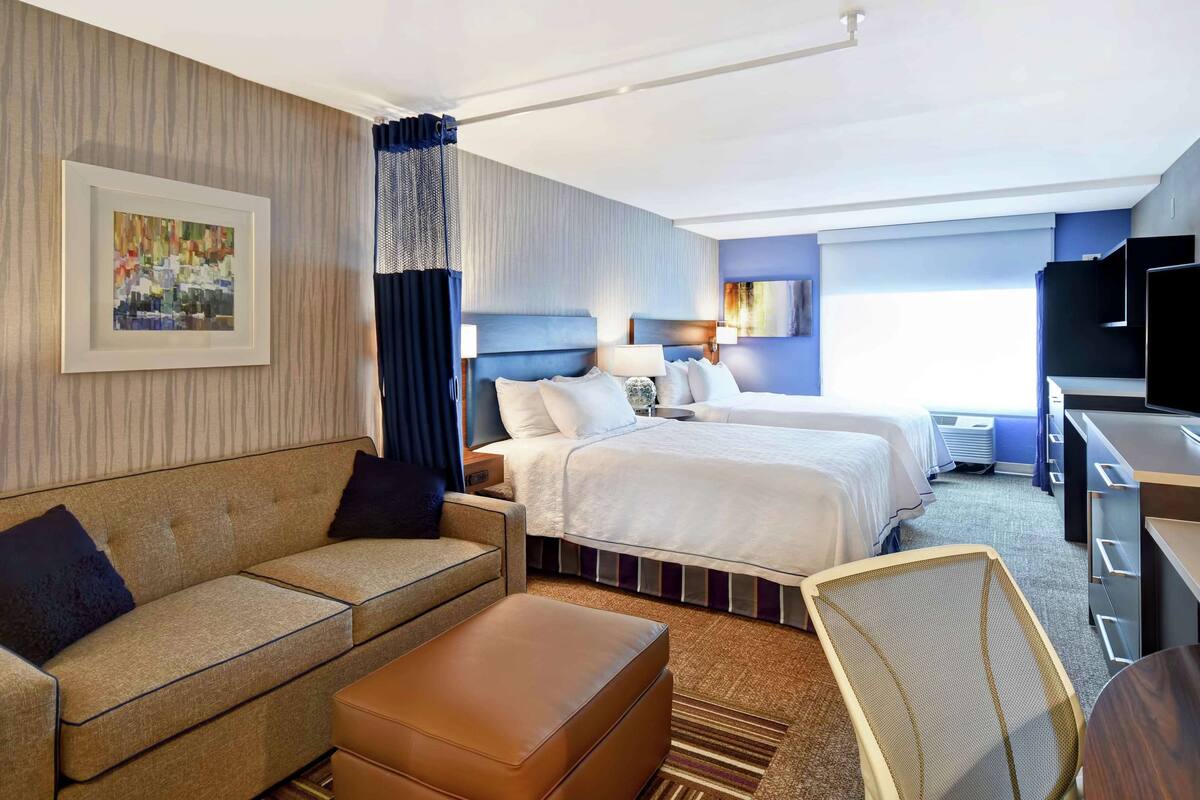 A hotel room with a bed, a sofa, a chair, a desk, and a television.