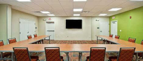 A conference room with a long table, chairs, a flat-screen TV, and carpeted flooring.