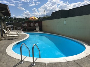 A swimming pool with a curved edge, surrounded by a low wall and a paved deck. There are lounge chairs and a small umbrella near the pool. - Cedars Inn Lewiston (Lewiston)