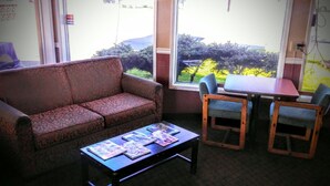 A room with a sofa, a coffee table with magazines, a small table with chairs, and a view of greenery outside.