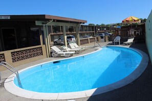 A swimming pool with lounge chairs, a covered area, and a parking lot with vehicles.