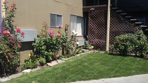 A building with a brown exterior, a small garden with pink and yellow flowers, and a wooden fence.