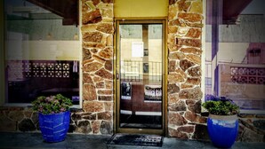 A stone building with a glass door, two blue planters with flowers, and a doormat.