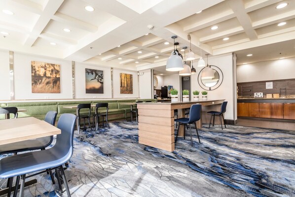 A modern hotel lobby with a central bar area, seating arrangements, and artwork on the walls.