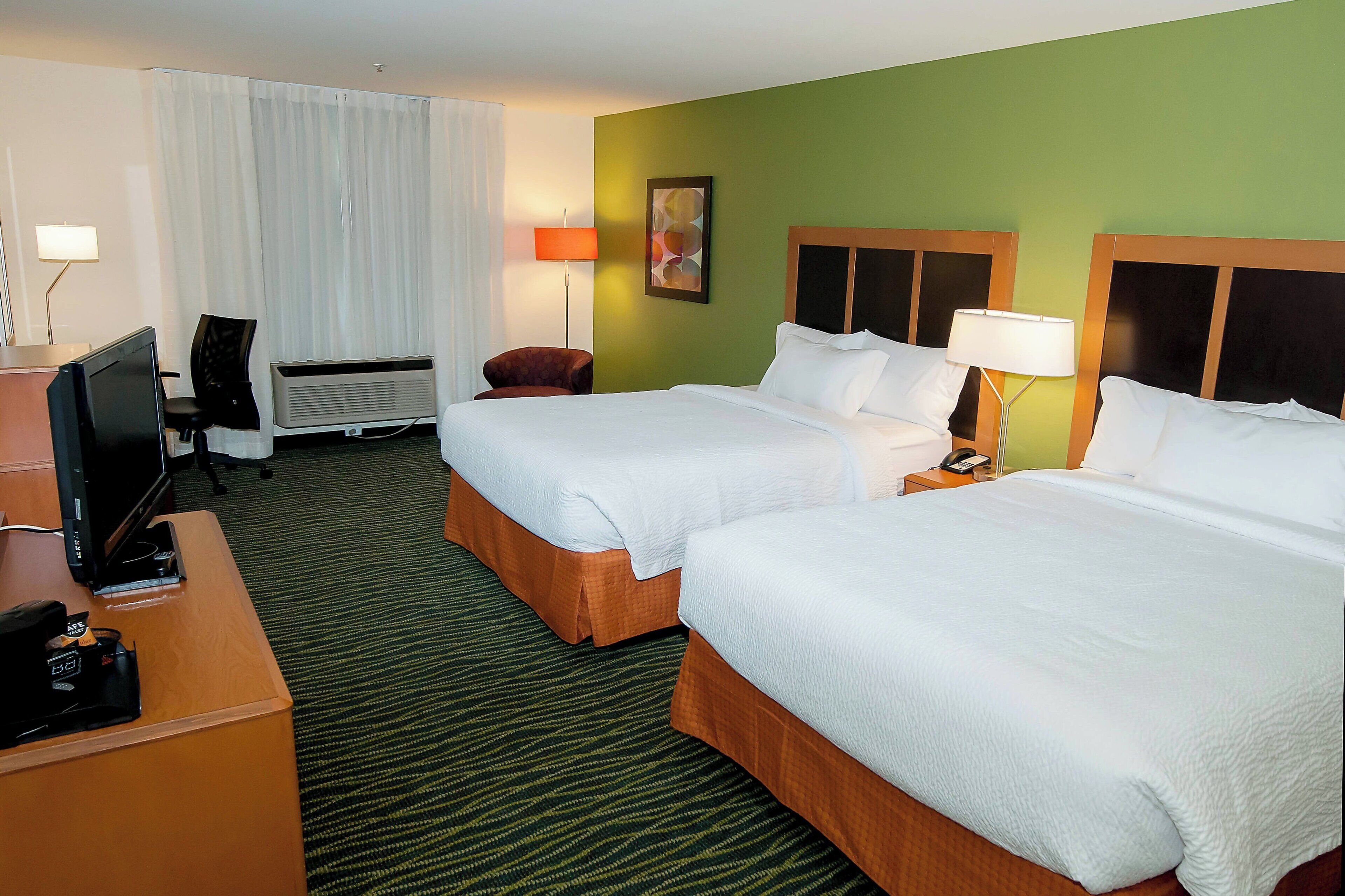 A hotel room with two beds, a desk with a computer, a chair, and a lamp.