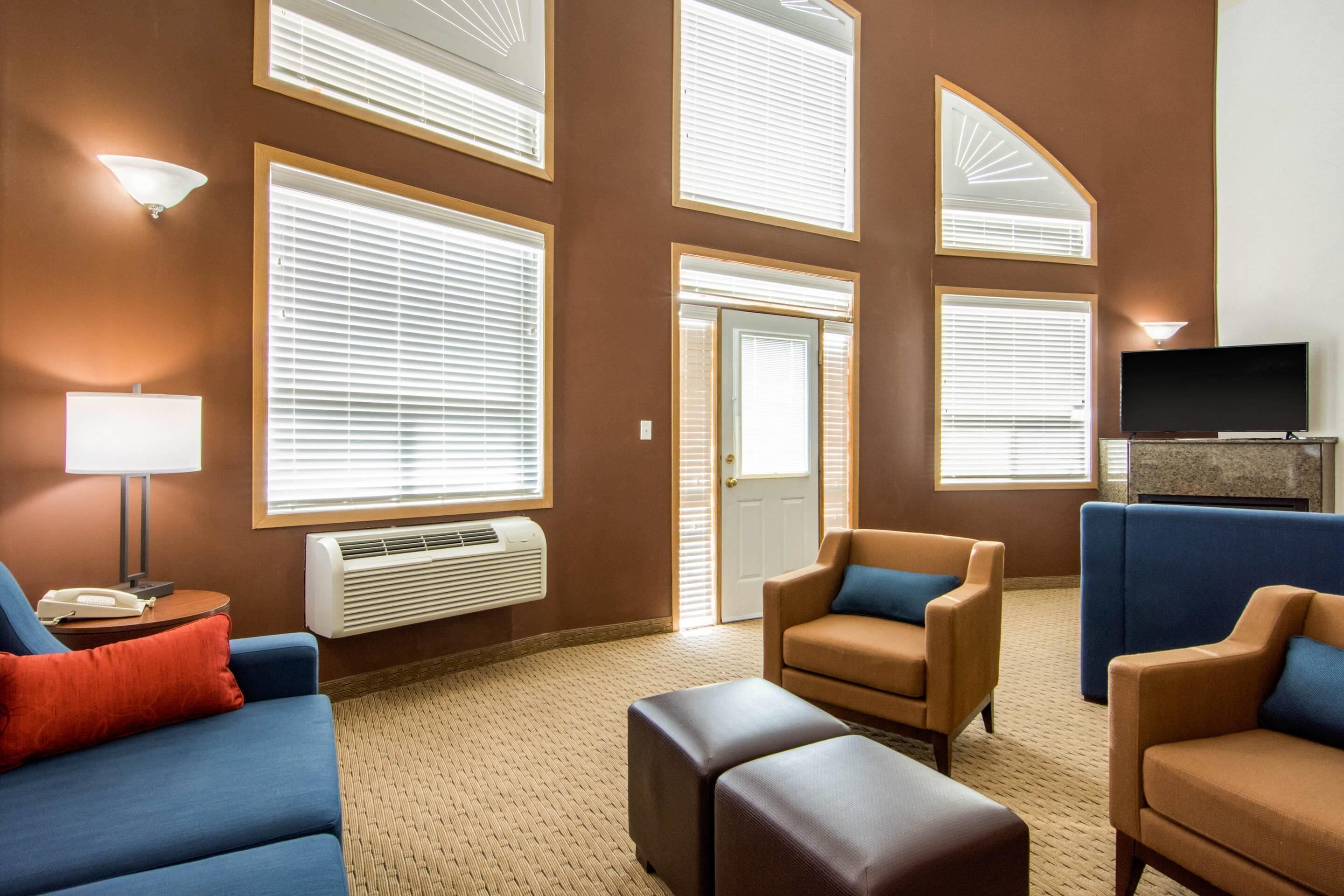 A hotel room with a large window, a flat-screen TV, and a seating area with sofas and ottomans.
