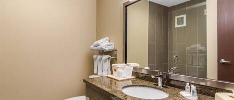 A hotel bathroom with a granite countertop, two sinks, a toilet, and a large mirror.
