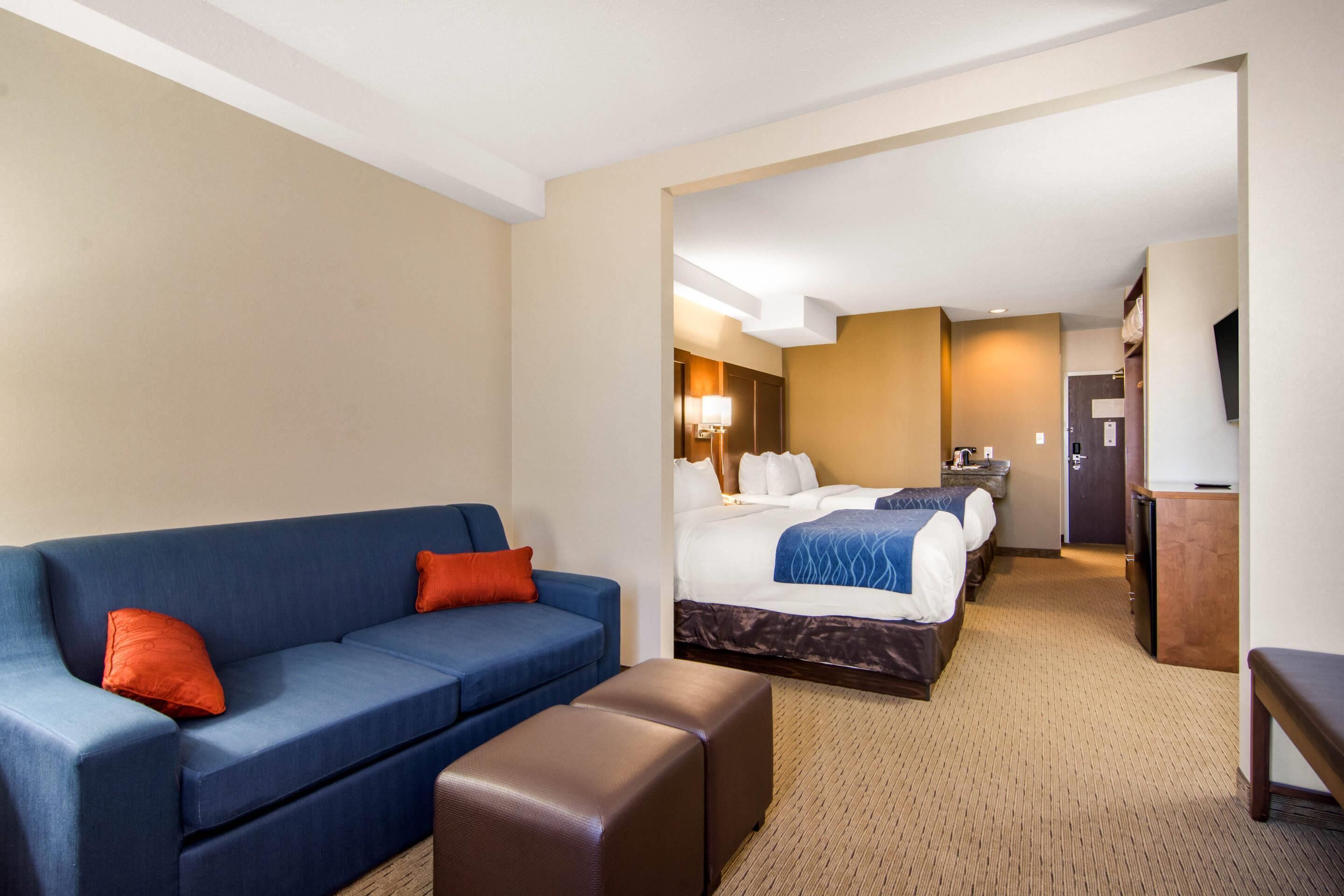 A hotel room with a blue sofa, a bed with a blue and white bedspread, a wooden bench, a desk with a lamp, and a television.