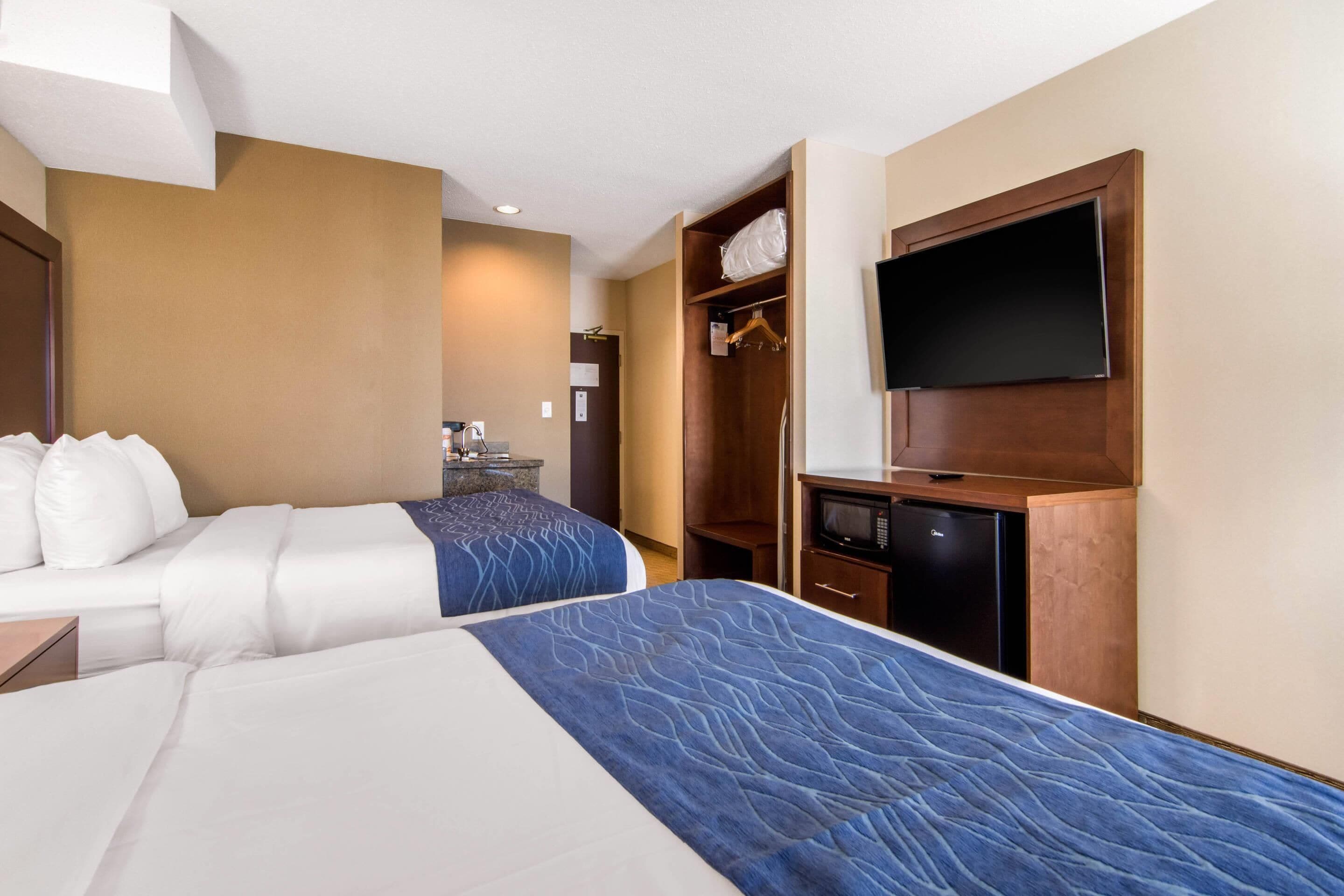 A hotel room with two beds, a TV, a wardrobe, and a microwave.
