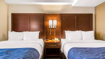 A hotel room with two beds, a nightstand with a phone and a lamp, and a wooden headboard.