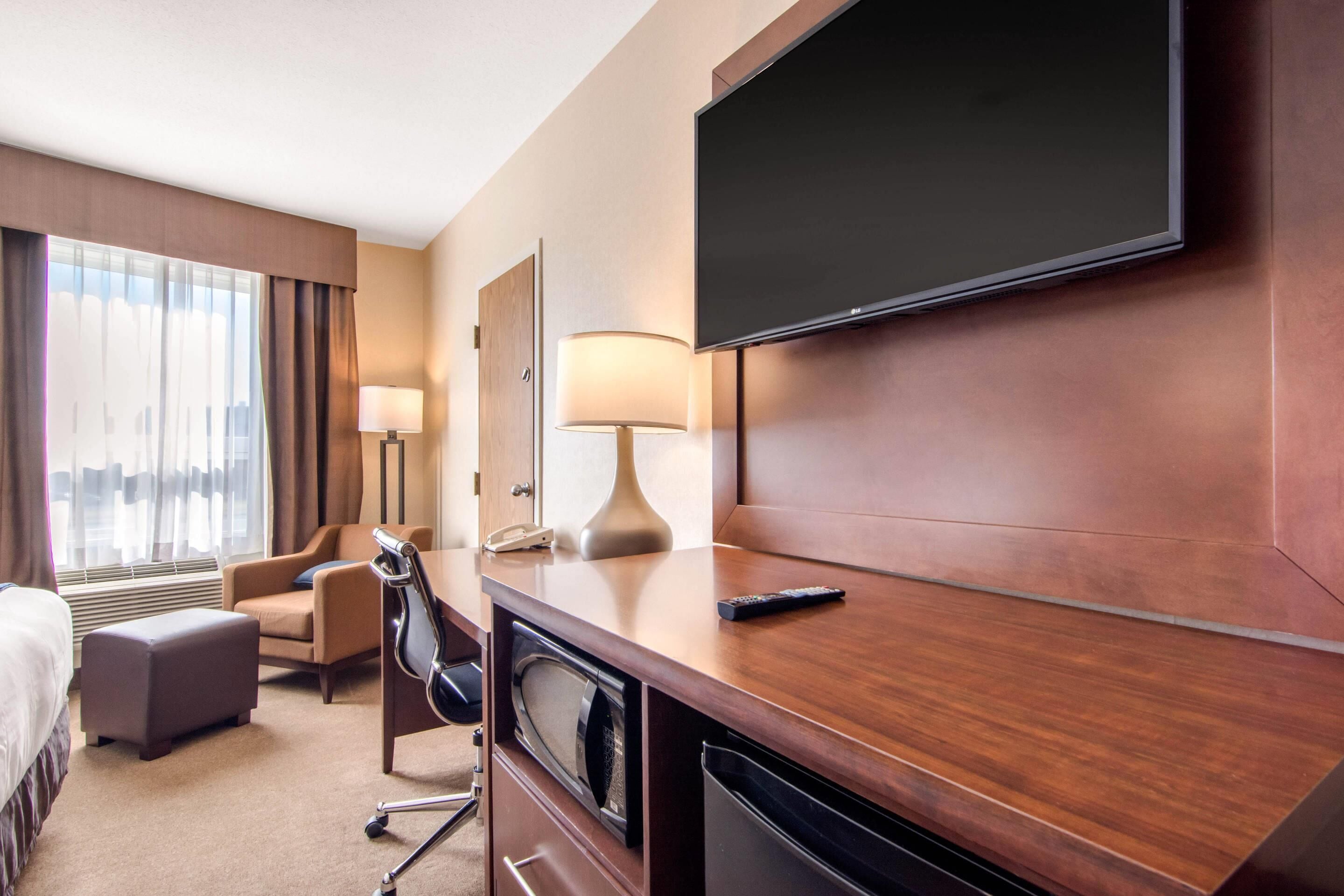 Une chambre d’hôtel équipée d’un lit, d’un bureau avec une lampe, d’une télévision, d’une chaise et d’un four à micro-ondes.