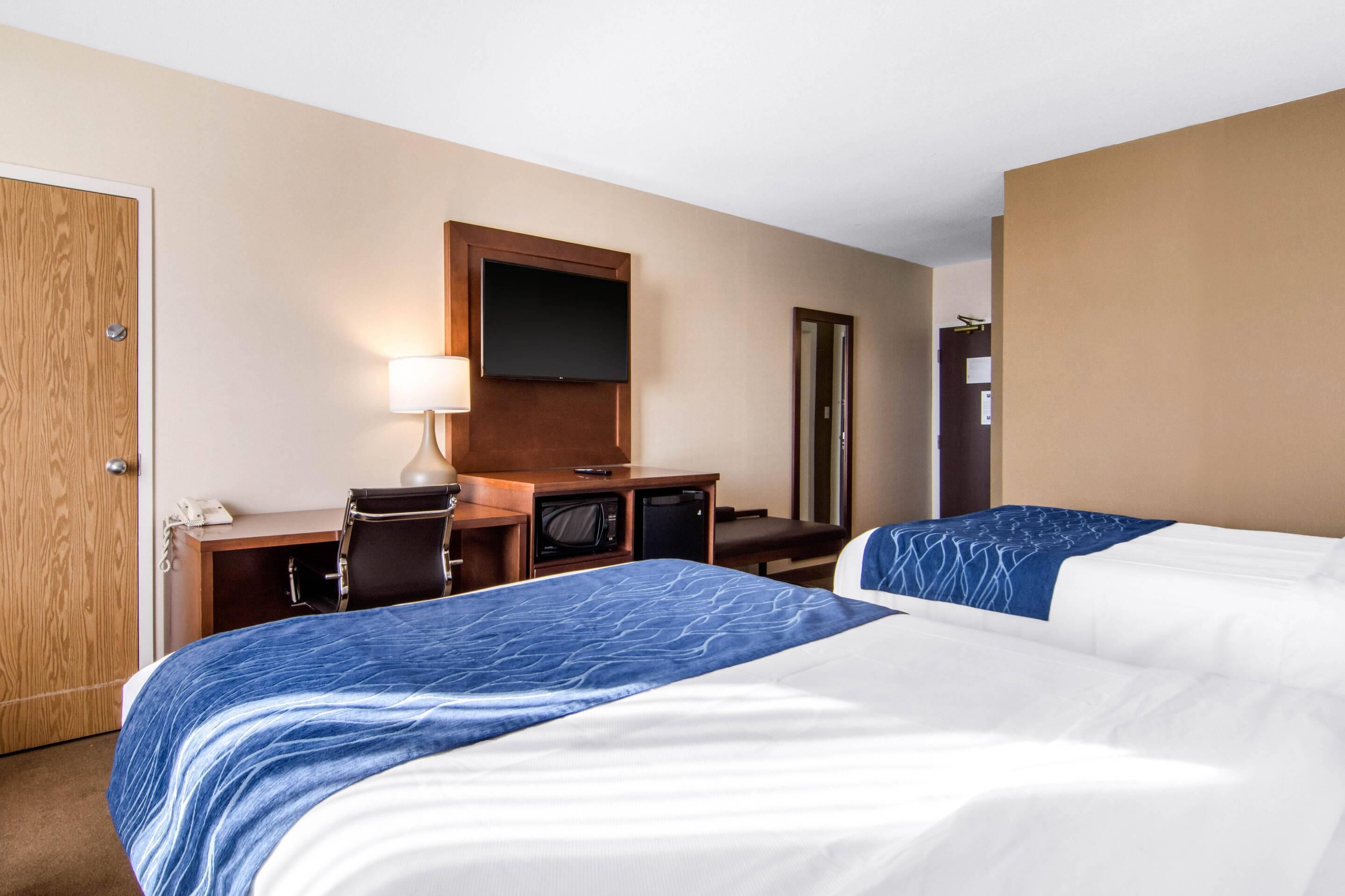 A hotel room with two beds, a desk, a television, and a mirror.