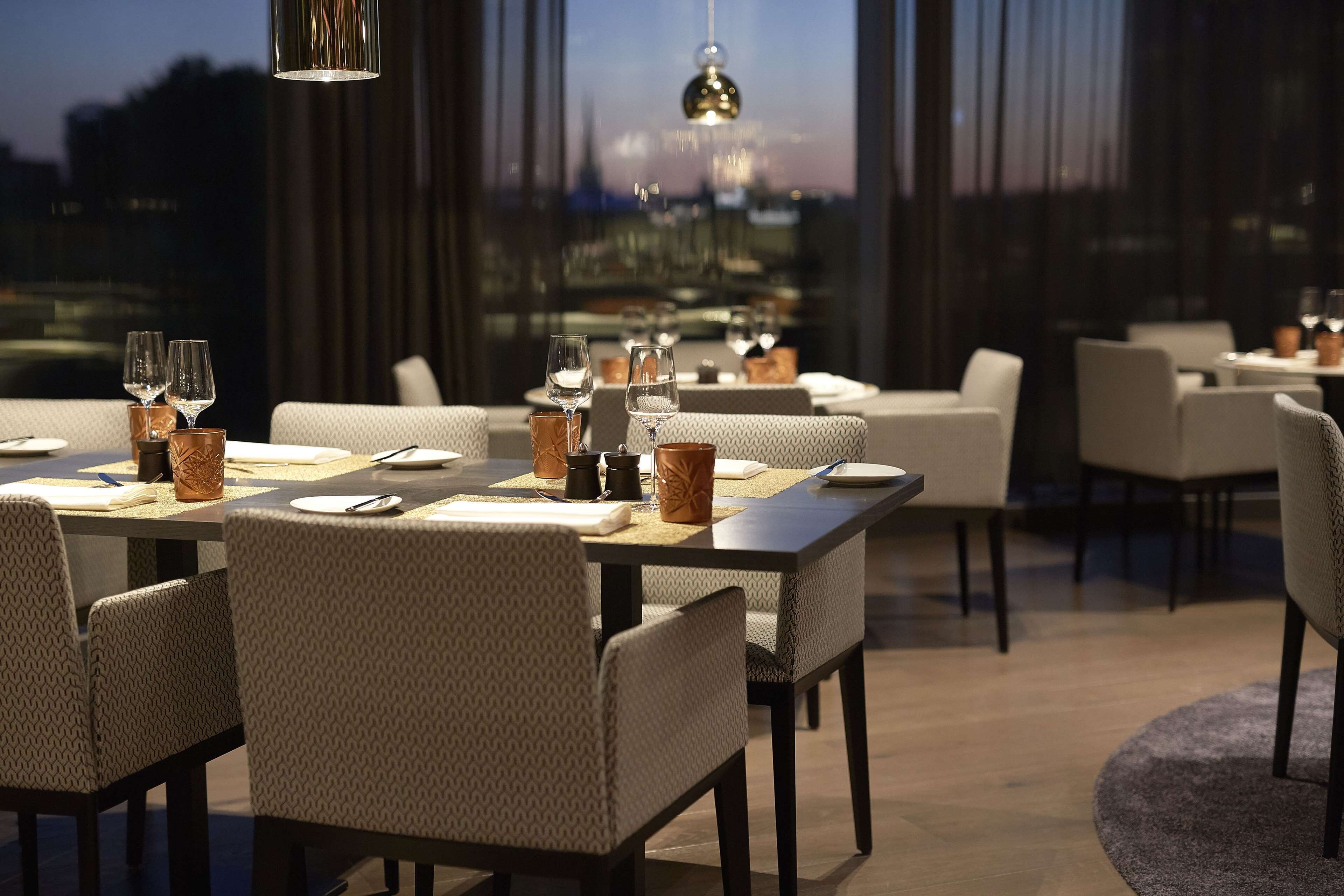 Uma sala de jantar moderna com mesas postas para o jantar, oferecendo vista da cidade por grandes janelas.