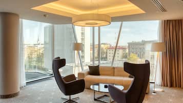 Una habitación de hotel moderna con un ventanal grande, un sofá, dos sillones y una mesa.