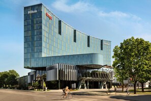 A modern hotel with a curved glass facade and a prominent Hilton logo. - Hilton Tallinn Park (Tallinn)